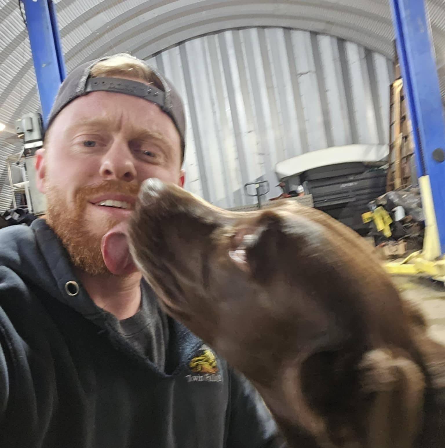 Jake Wall in his shop, getting a face full of enthusiasm from his dog, Uzi.